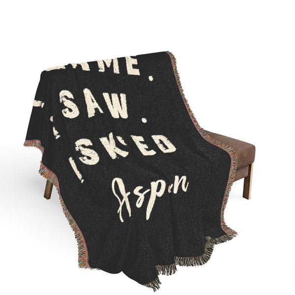 A black woven throw blanket with cream-colored distressed text reading 'I SAW. I SKIED.